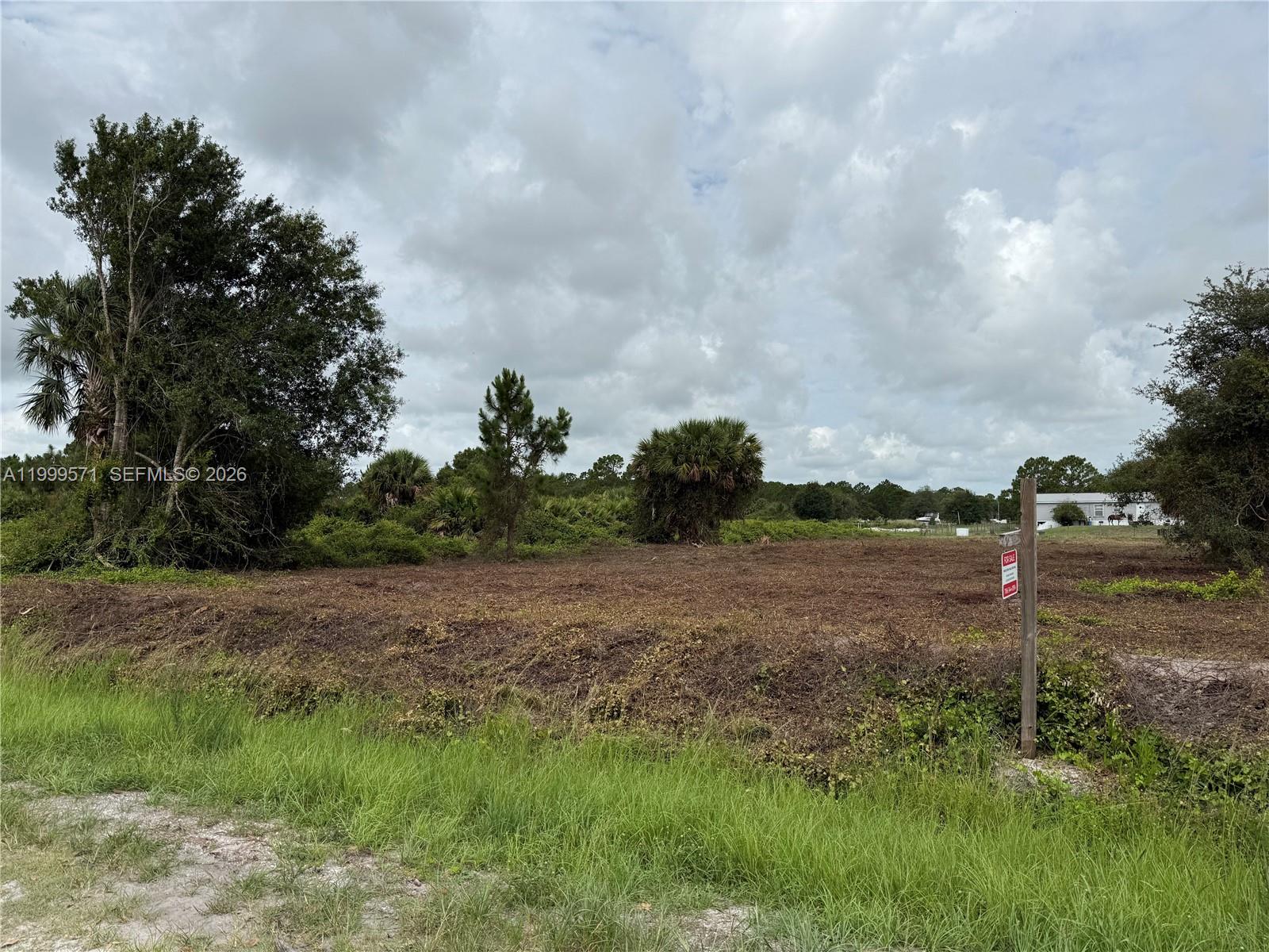 A vacant, cleared lot features scattered trees and a for-sale sign under a cloudy sky — 760 N NOGAL ST, Clewiston FL 33440, CLEWISTON, FL