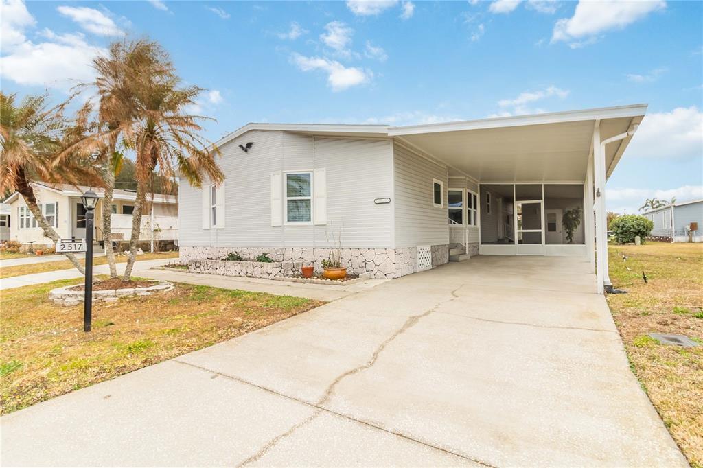 A light-colored manufactured home features a concrete driveway, a carport, and a stone-textured foundation — 2517 INDEPENDENCE LANE, ST CLOUD, FL