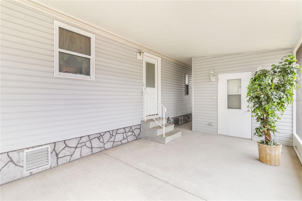 A covered patio features light gray vinyl siding, stone-patterned skirting, and two white entry doors — 2517 INDEPENDENCE LANE, ST CLOUD, FL
