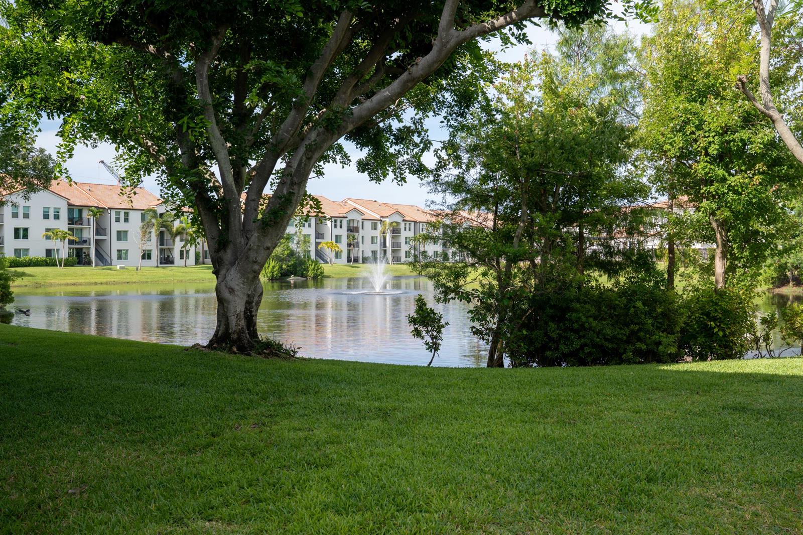 A pond with a fountain sits in front of apartment buildings surrounded by green trees — 809 Villa Circle, Boynton Beach FL 33435, BOYNTON BEACH, FL