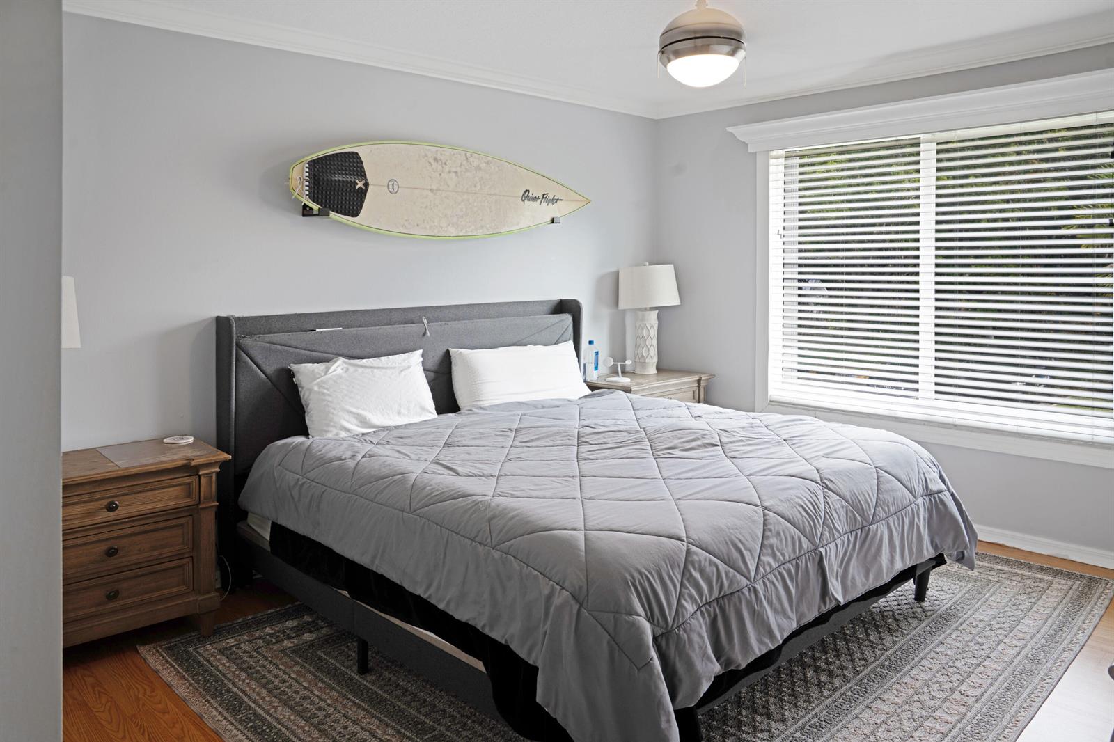 A bedroom features a gray upholstered bed, a surfboard wall decoration, and a window with blinds — 809 Villa Circle, Boynton Beach FL 33435, BOYNTON BEACH, FL