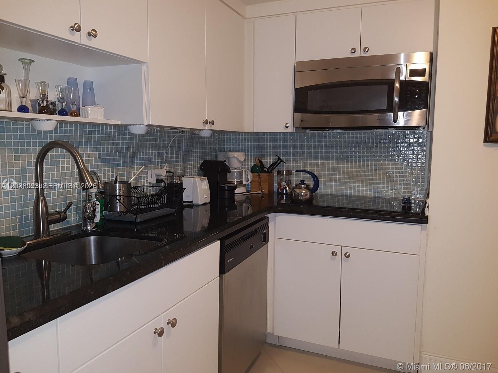 A kitchen features white cabinets, black countertops, stainless steel appliances, and a blue tiled backsplash — 801 Brickell Bay Dr # 765, Miami FL 33131, MIAMI, FL