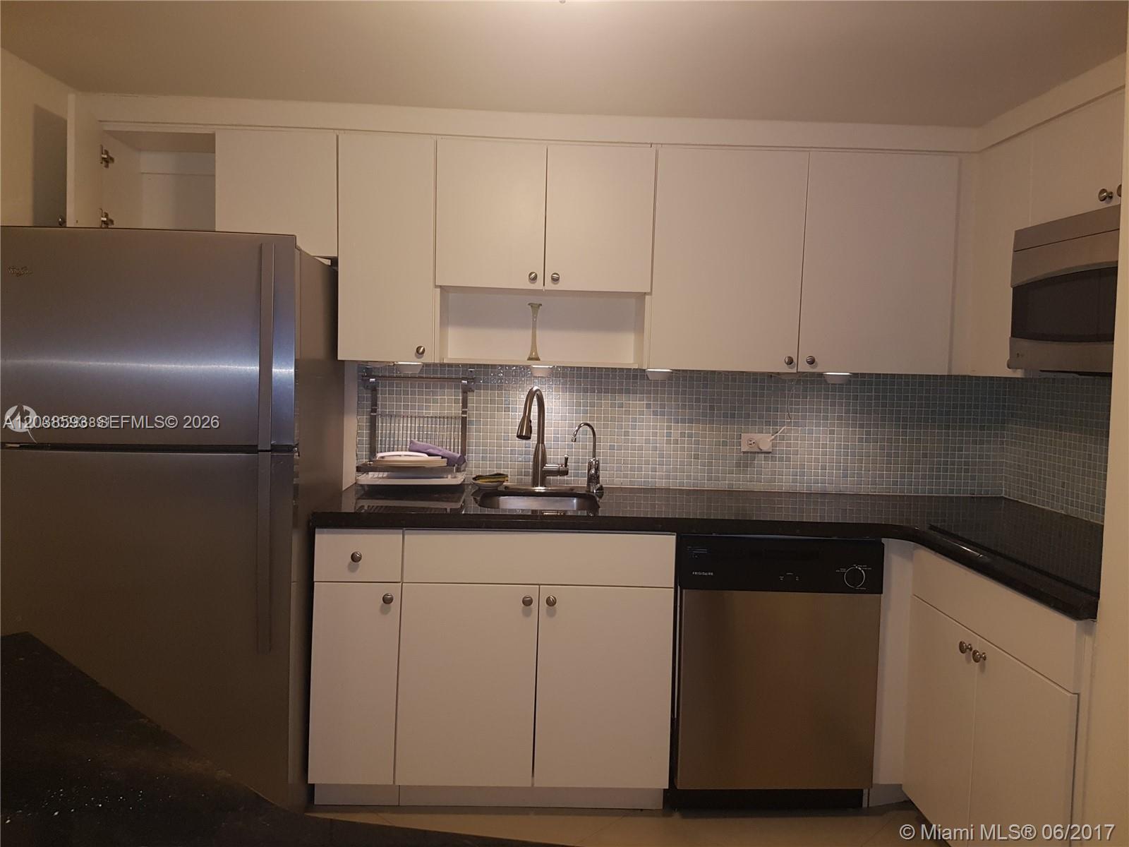 A kitchen features white cabinets, stainless steel appliances, a black countertop, and a tiled backsplash — 801 Brickell Bay Dr # 765, Miami FL 33131, MIAMI, FL