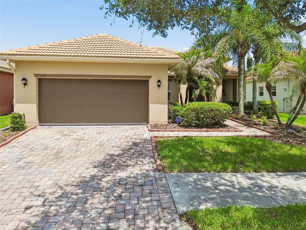 A single-story house with a tan stucco exterior, a paved driveway, and a two-car garage — 518 DAVINCI PASS, KISSIMMEE, FL