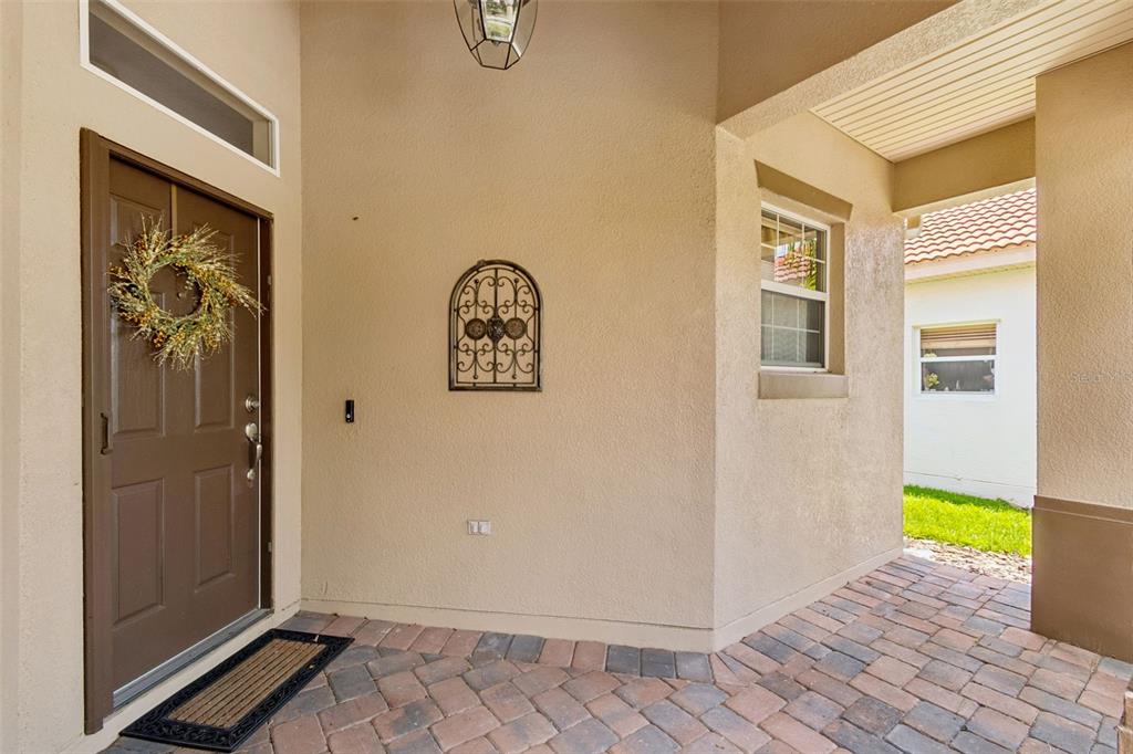 A covered entryway features a brown front door, a decorative wall hanging, and paver flooring — 518 DAVINCI PASS, KISSIMMEE, FL