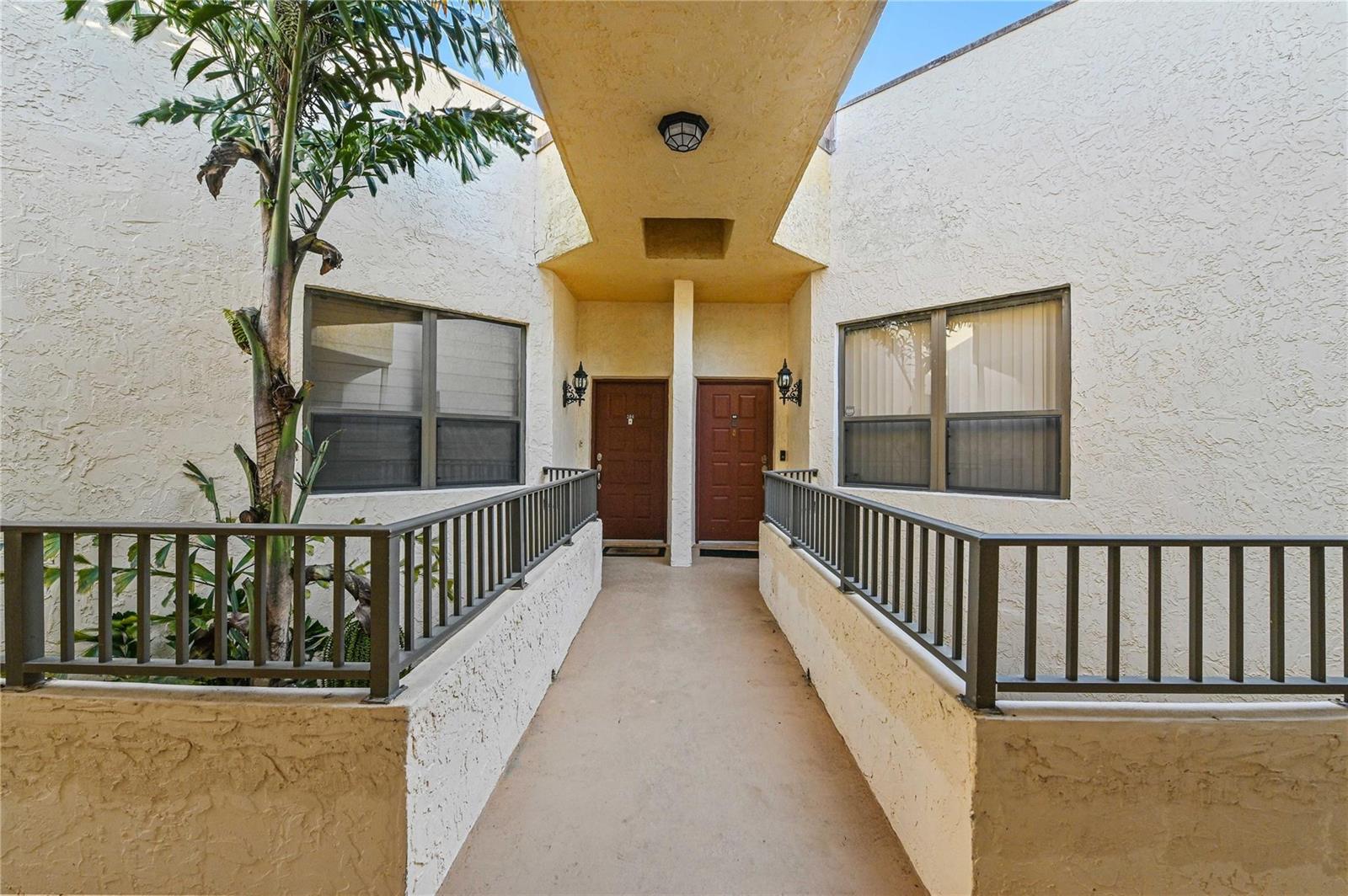 An exterior walkway leads to two brown front doors between stucco walls and metal railings — 7520 La Paz Boulevard # 306, Boca Raton FL 33433, BOCA RATON, FL