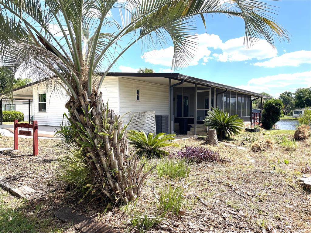 A white mobile home features a screened-in porch and a palm tree in the yard — 2 GROVE TRAIL, WILDWOOD, FL
