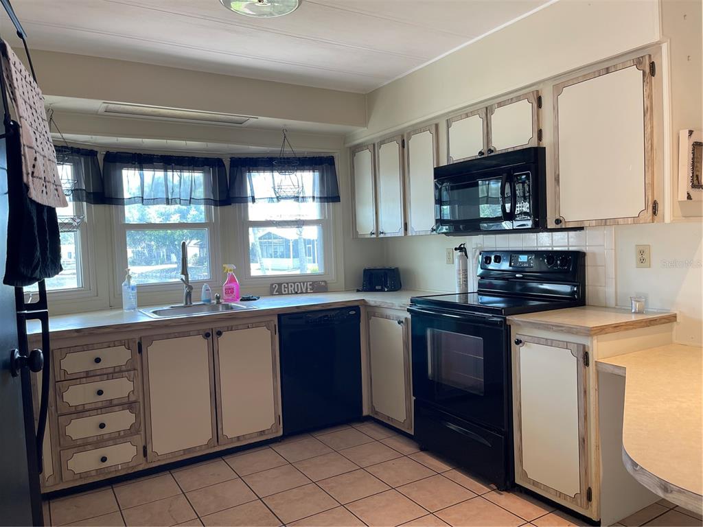 A kitchen features light-colored cabinets with dark trim, black appliances, and a tiled floor — 2 GROVE TRAIL, WILDWOOD, FL