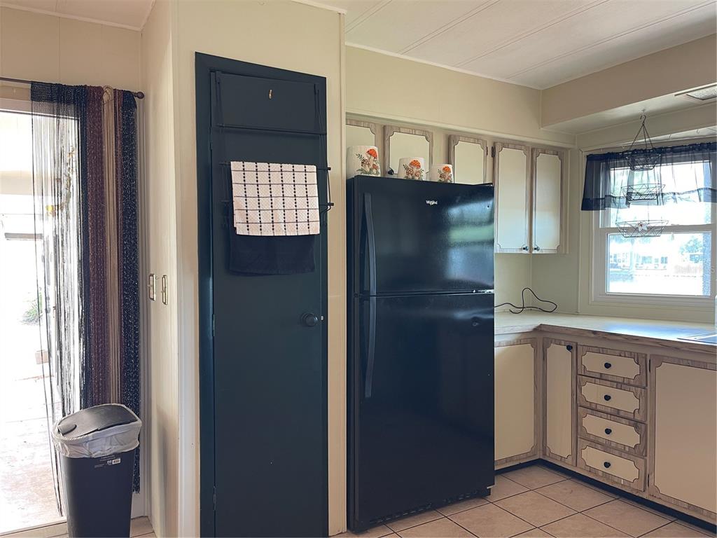 A kitchen features a black refrigerator, a dark pantry door, and light-colored cabinetry — 2 GROVE TRAIL, WILDWOOD, FL
