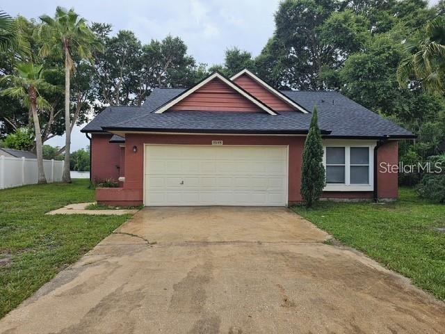 A single-story house with a two-car garage, red siding, and a dark shingled roof — 10148 PINK CARNATION COURT, ORLANDO, FL