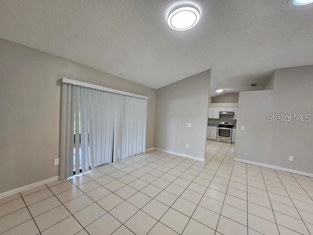 A room with light-colored tile flooring, vertical blinds on a sliding door, and an open kitchen — 10148 PINK CARNATION COURT, ORLANDO, FL