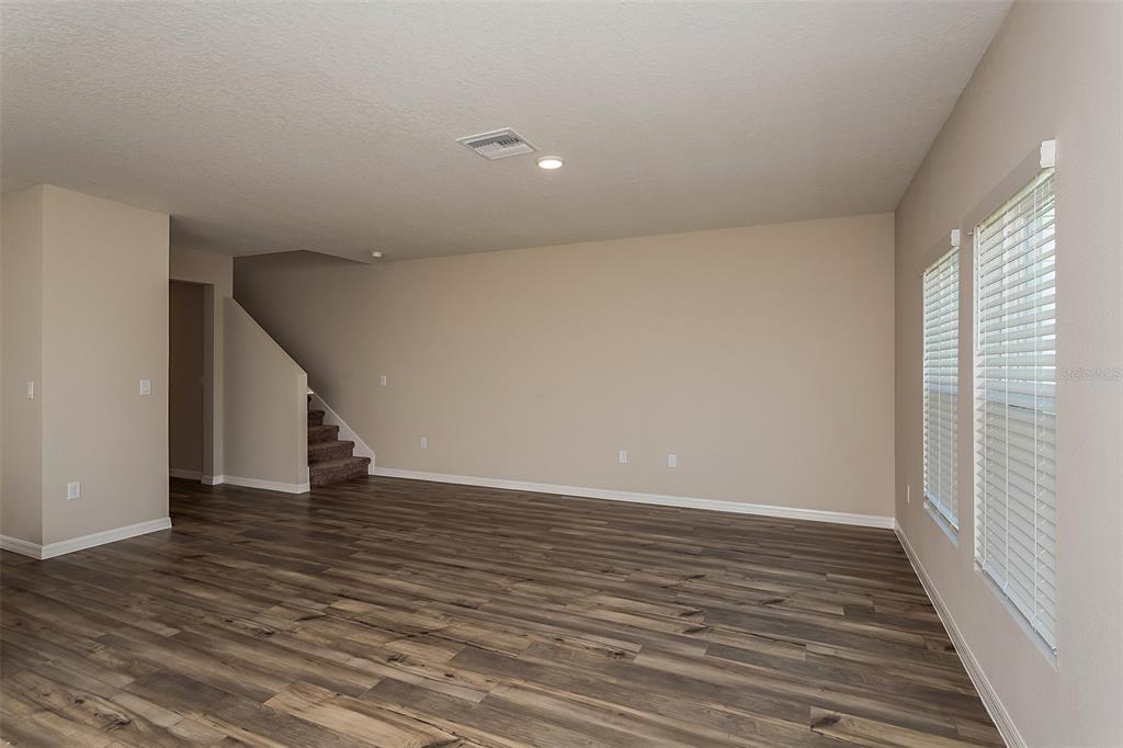 An empty living room features wood-look flooring, beige walls, and a staircase in the background — 33569 NOBLE CREEK PLACE, DADE CITY, FL