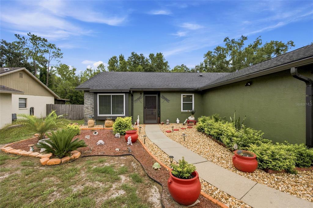 A single-story house with green stucco walls, a gray shingled roof, and a landscaped front yard — 5016 SWALLOW DRIVE, LAND O LAKES, FL