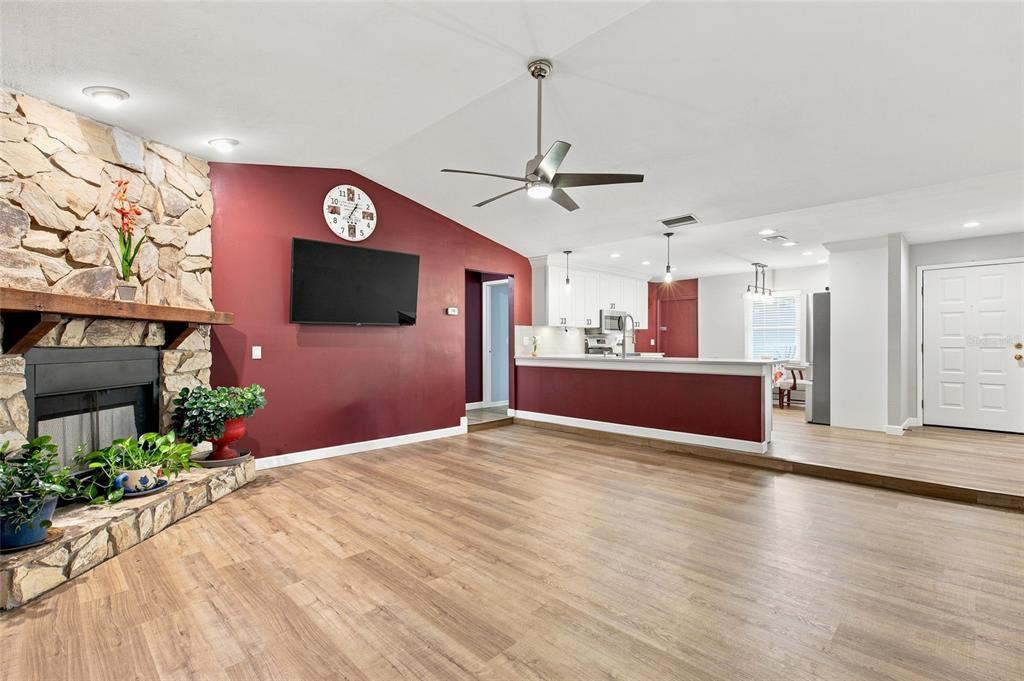 A living room with a stone fireplace, red accent wall, and an open kitchen — 5016 SWALLOW DRIVE, LAND O LAKES, FL