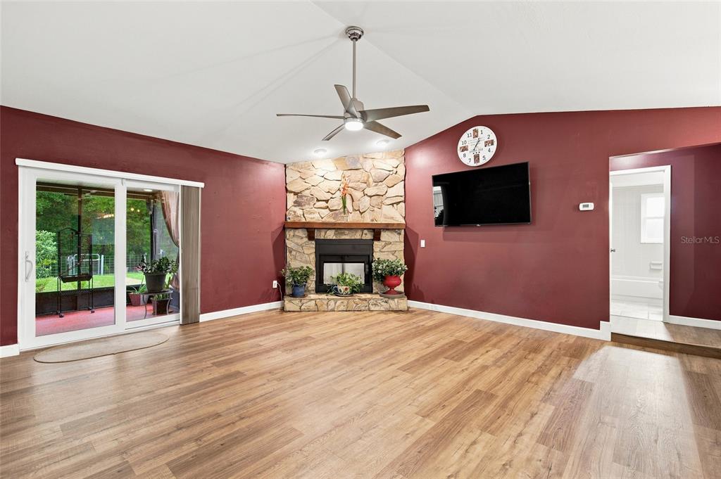 A living room features wood-look flooring, a stone fireplace, a ceiling fan, and red walls — 5016 SWALLOW DRIVE, LAND O LAKES, FL