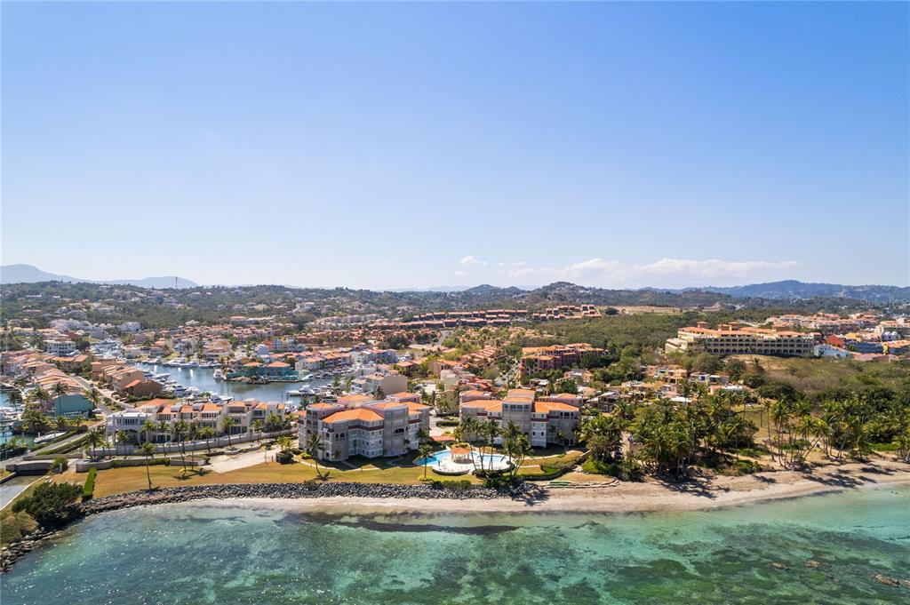 An aerial view shows beachfront residential buildings with a pool near a coastal marina — 355 HARBOUR DR UNIT 3C - South, HUMACAO, PR