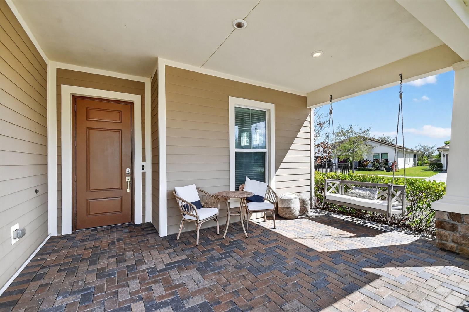 A covered front porch features a brick paver floor, a swing, and two chairs — 19535 Split Rail Run, Loxahatchee FL 33470, LOXAHATCHEE, FL