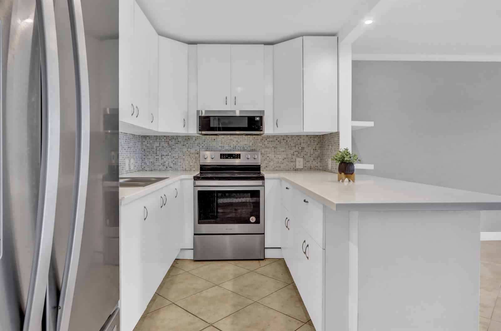 A kitchen features white cabinets, stainless steel appliances, a mosaic tile backsplash, and tile flooring — 265 Preston G Way # 265, Boca Raton FL 33434, BOCA RATON, FL