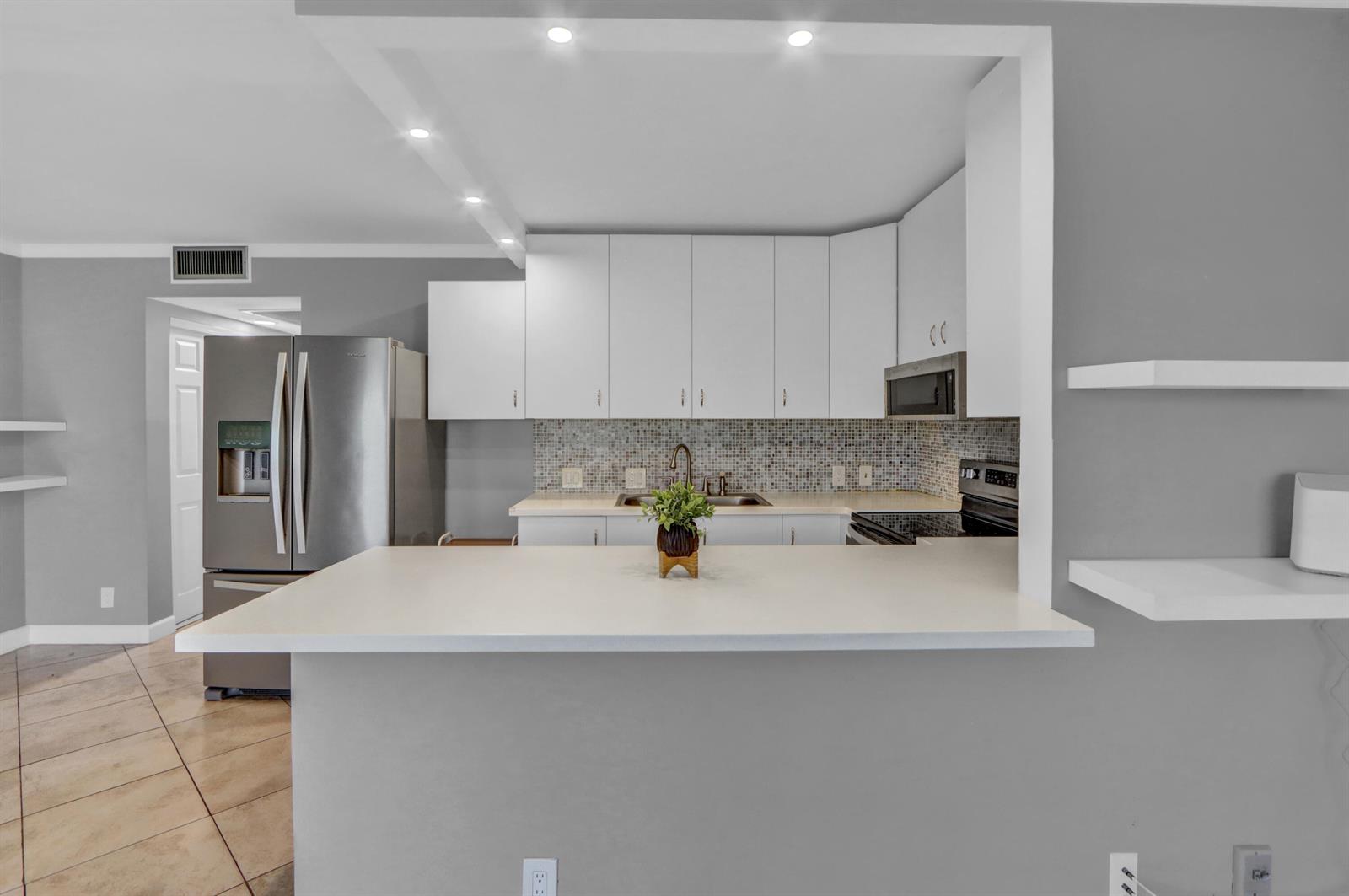 A kitchen features white cabinets, a mosaic tile backsplash, stainless steel appliances, and a breakfast bar — 265 Preston G Way # 265, Boca Raton FL 33434, BOCA RATON, FL