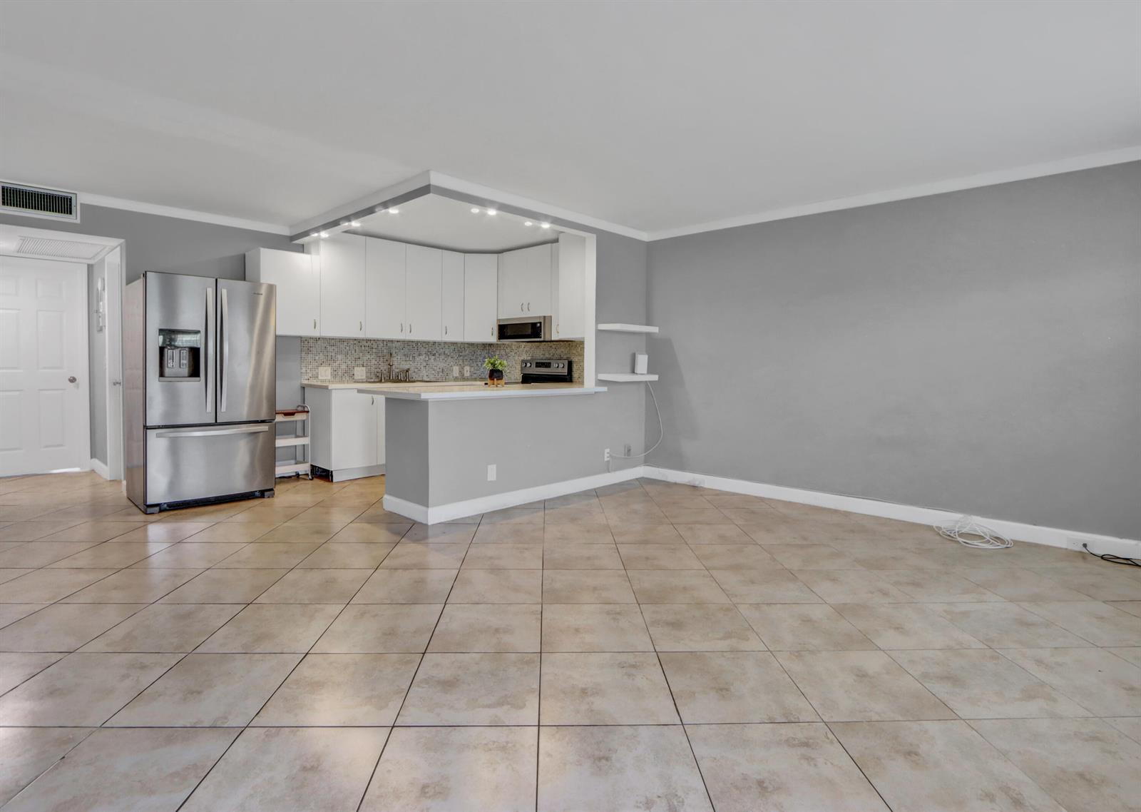 A kitchen with white cabinets and stainless steel appliances opens to a tiled living area — 265 Preston G Way # 265, Boca Raton FL 33434, BOCA RATON, FL