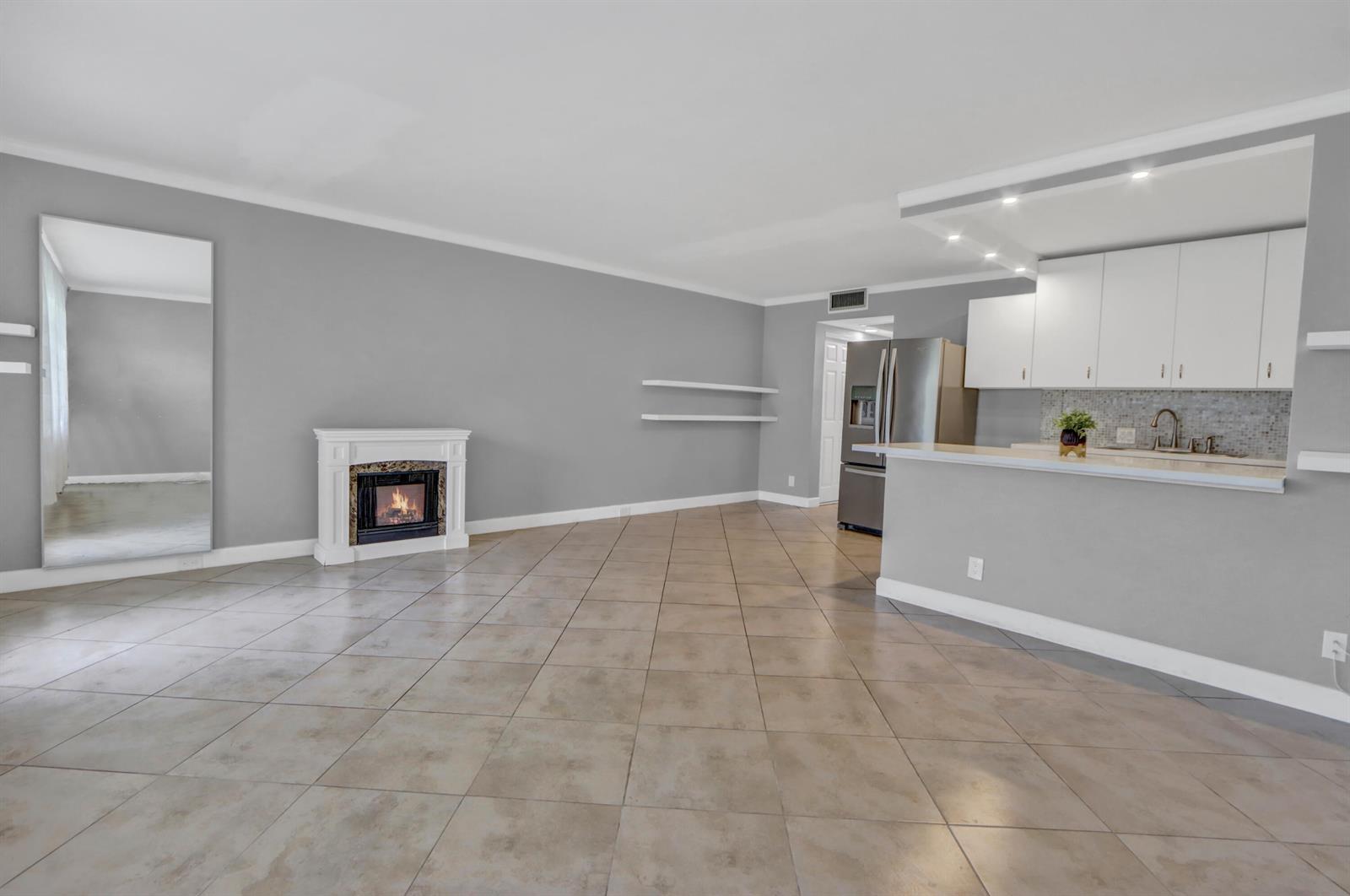 An open-concept living room features tile flooring, a fireplace, and an adjacent kitchen with white cabinets — 265 Preston G Way # 265, Boca Raton FL 33434, BOCA RATON, FL
