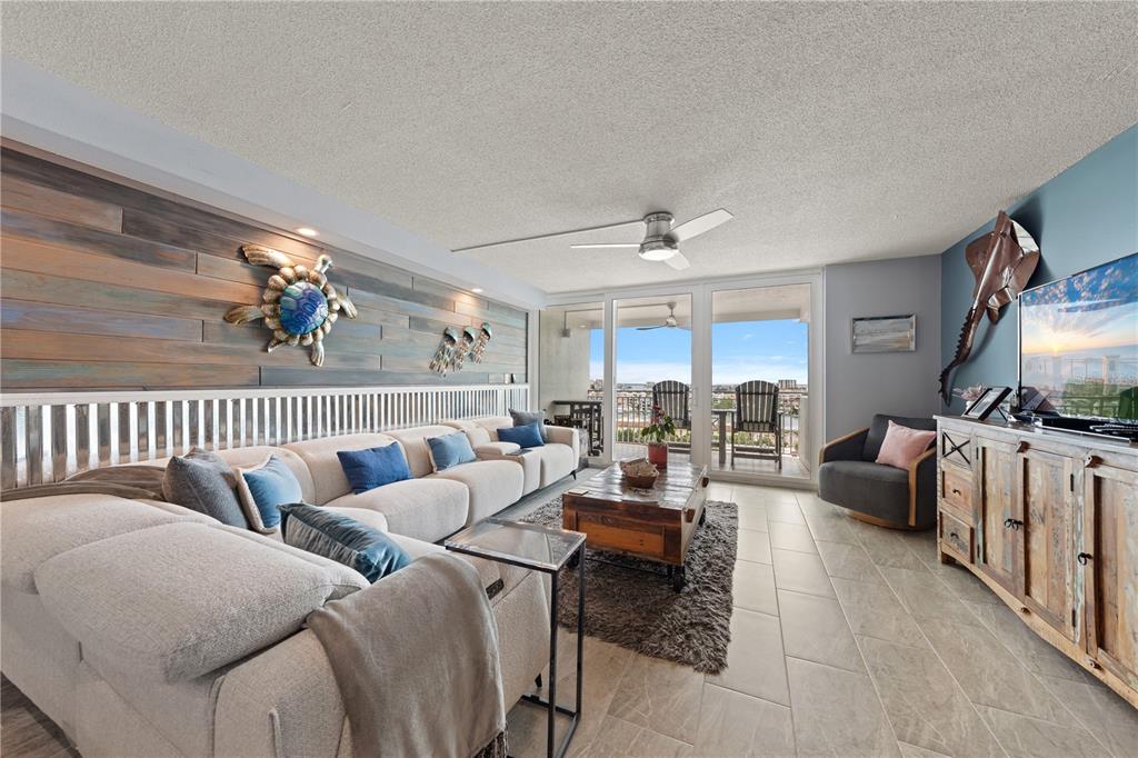 A living room features a large sectional sofa, wood-paneled wall, and a balcony with views — 675 S GULFVIEW BOULEVARD UNIT 1108, CLEARWATER BEACH, FL