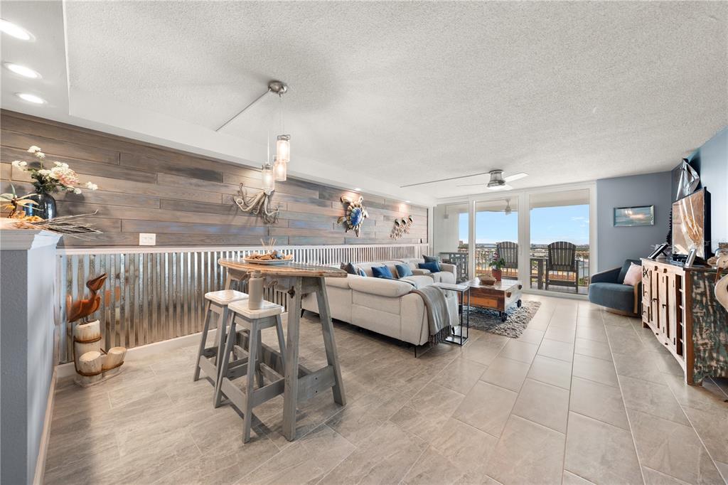 A living and dining area features wood-paneled walls, corrugated metal wainscoting, and a balcony view — 675 S GULFVIEW BOULEVARD UNIT 1108, CLEARWATER BEACH, FL