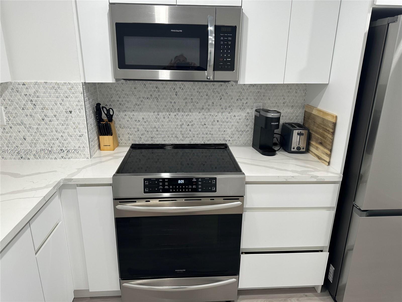 A modern kitchen features white cabinets, stainless steel appliances, and a geometric tile backsplash — 2655 Collins Ave # 608, Miami Beach FL 33140, MIAMI BEACH, FL