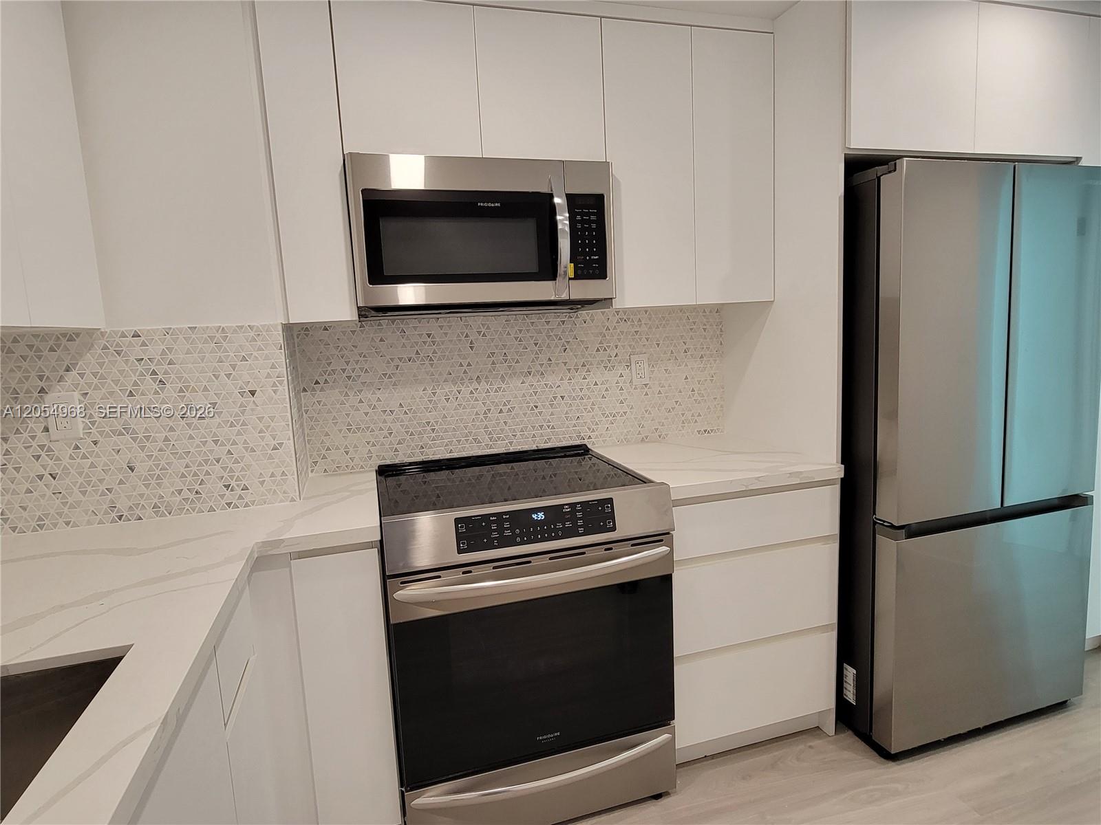 A modern kitchen features white cabinets, stainless steel appliances, and a geometric patterned tile backsplash — 2655 Collins Ave # 608, Miami Beach FL 33140, MIAMI BEACH, FL