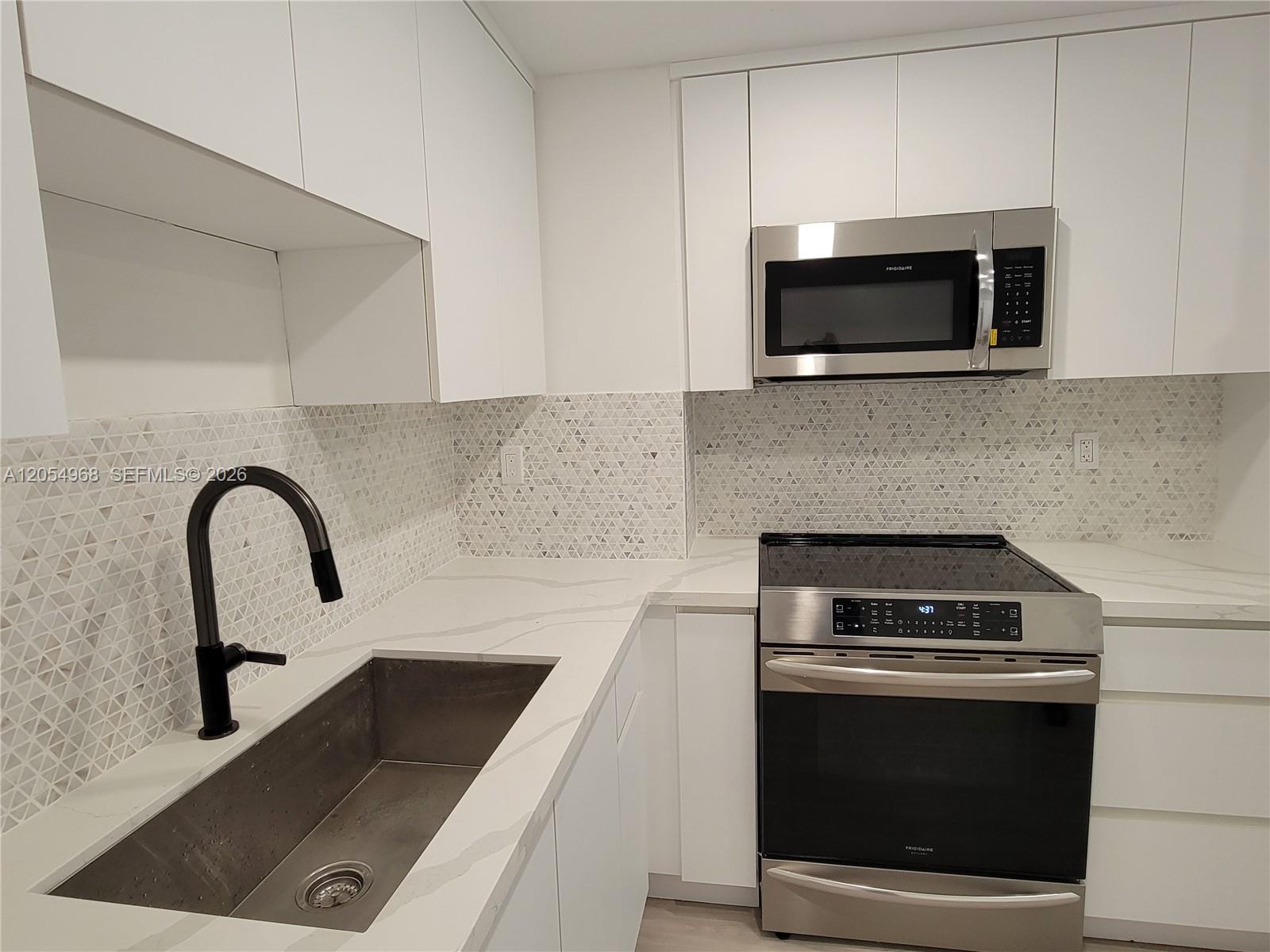 A modern kitchen features white cabinets, a stainless steel stove, and a geometric tile backsplash — 2655 Collins Ave # 608, Miami Beach FL 33140, MIAMI BEACH, FL