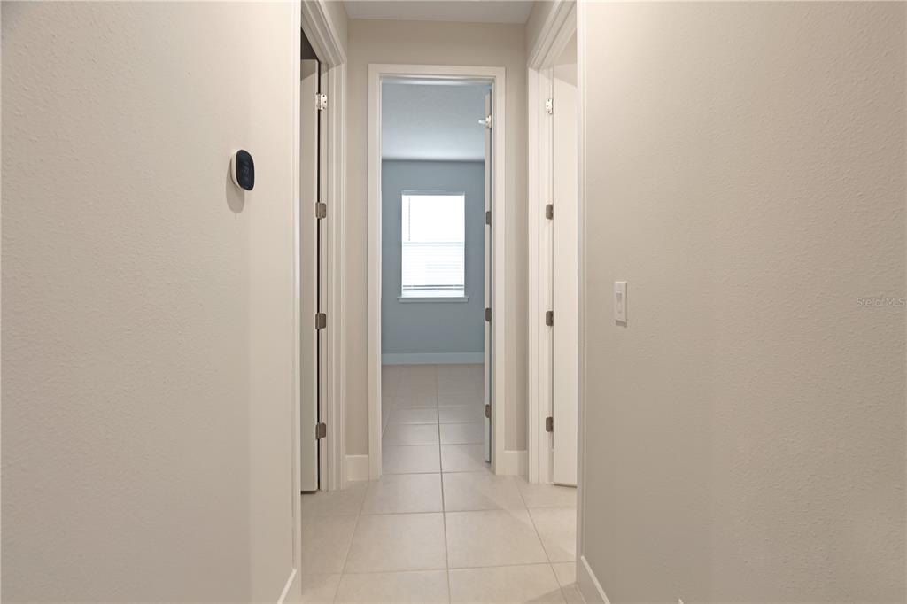 A hallway with light-colored tile flooring leads to a bedroom with a window — 17982 GRAND PROSPERITY DRIVE, VENICE, FL
