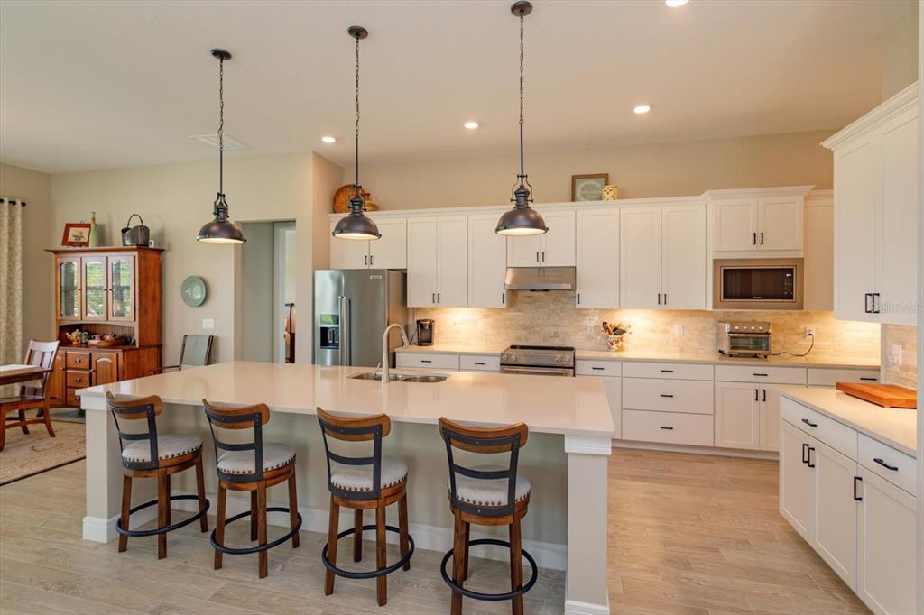 A modern kitchen features white cabinetry, a large quartz island with bar stools, and pendant lighting — 5663 SW 92ND AVENUE ROAD, OCALA, FL