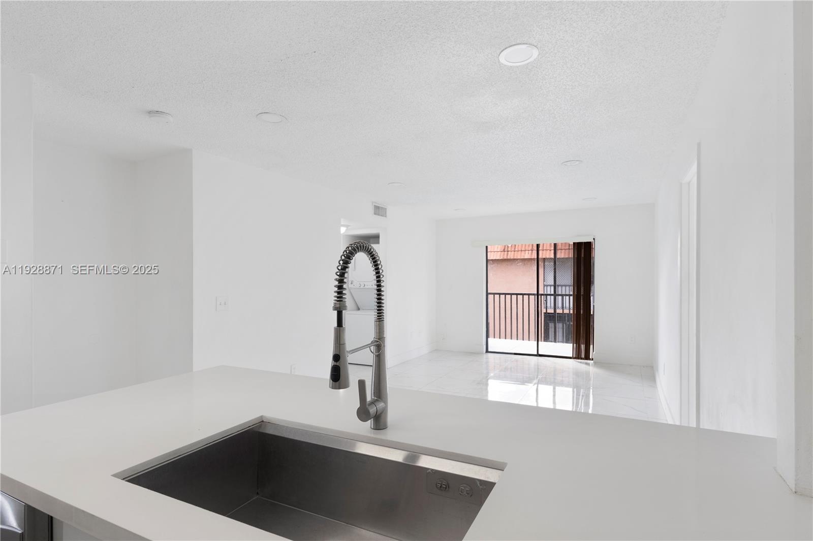 A kitchen sink with a gooseneck faucet overlooks a bright, open-concept living area — 6580 W 27th Ct # 21, Hialeah FL 33016, HIALEAH, FL