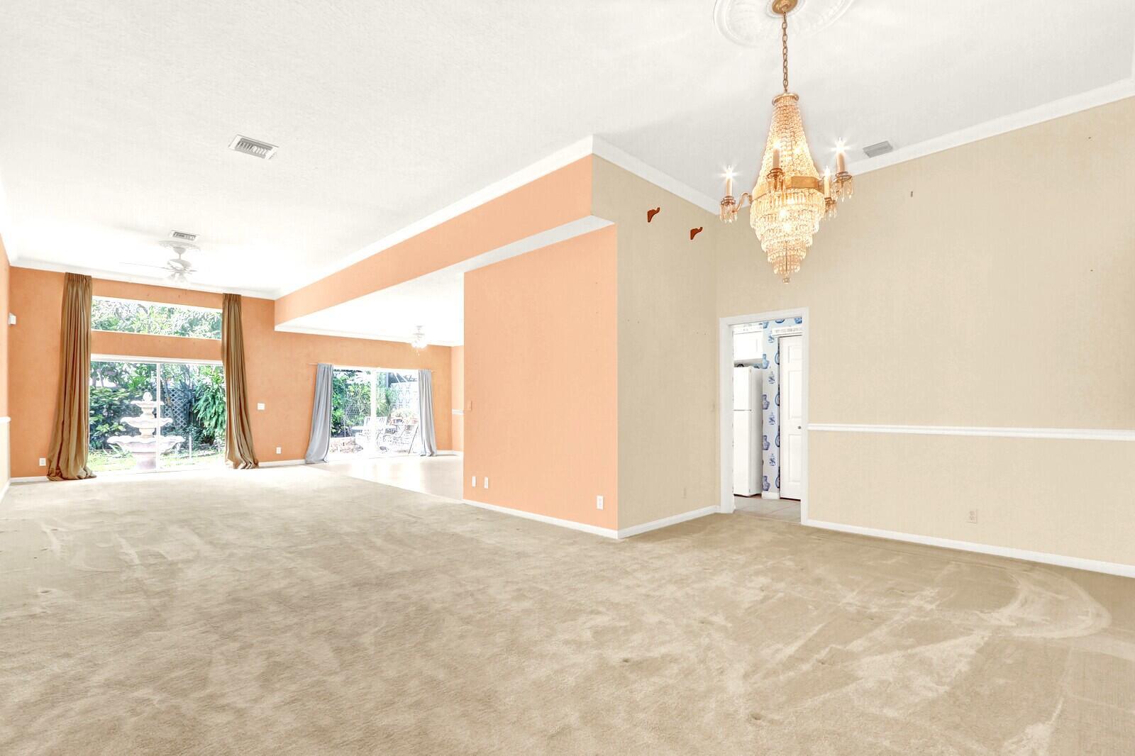 A spacious living room features beige carpeting, peach-colored walls, a crystal chandelier, and large windows — 3167 El Camino, West Palm Beach FL 33409, WEST PALM BEACH, FL