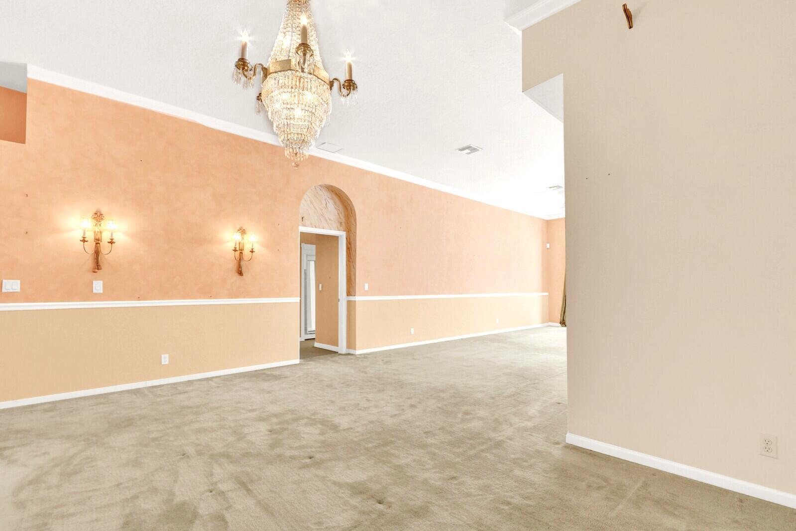 A spacious room features peach-colored walls, a crystal chandelier, wall sconces, and beige carpeting — 3167 El Camino, West Palm Beach FL 33409, WEST PALM BEACH, FL