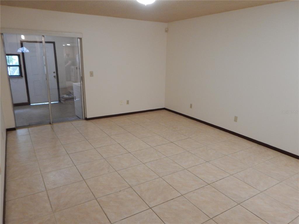 An empty room with beige tile flooring and a sliding glass door leading outside — 2505 CORAL AVENUE, KISSIMMEE, FL