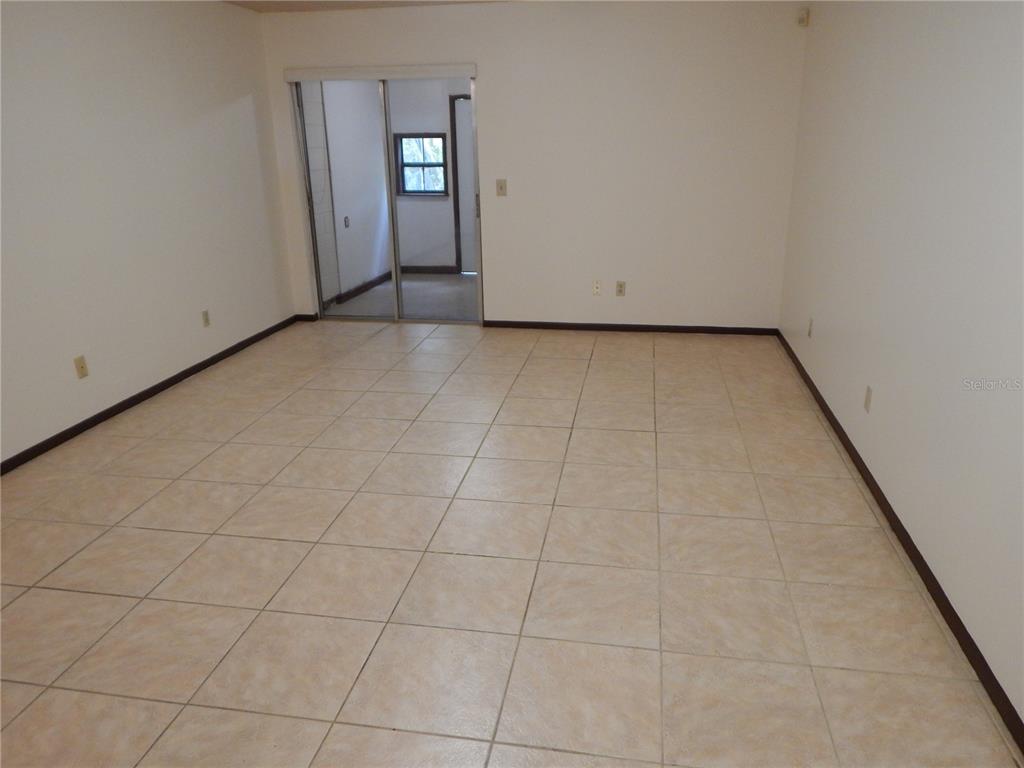 An empty room with beige tile flooring and a sliding glass door leading outside — 2505 CORAL AVENUE, KISSIMMEE, FL
