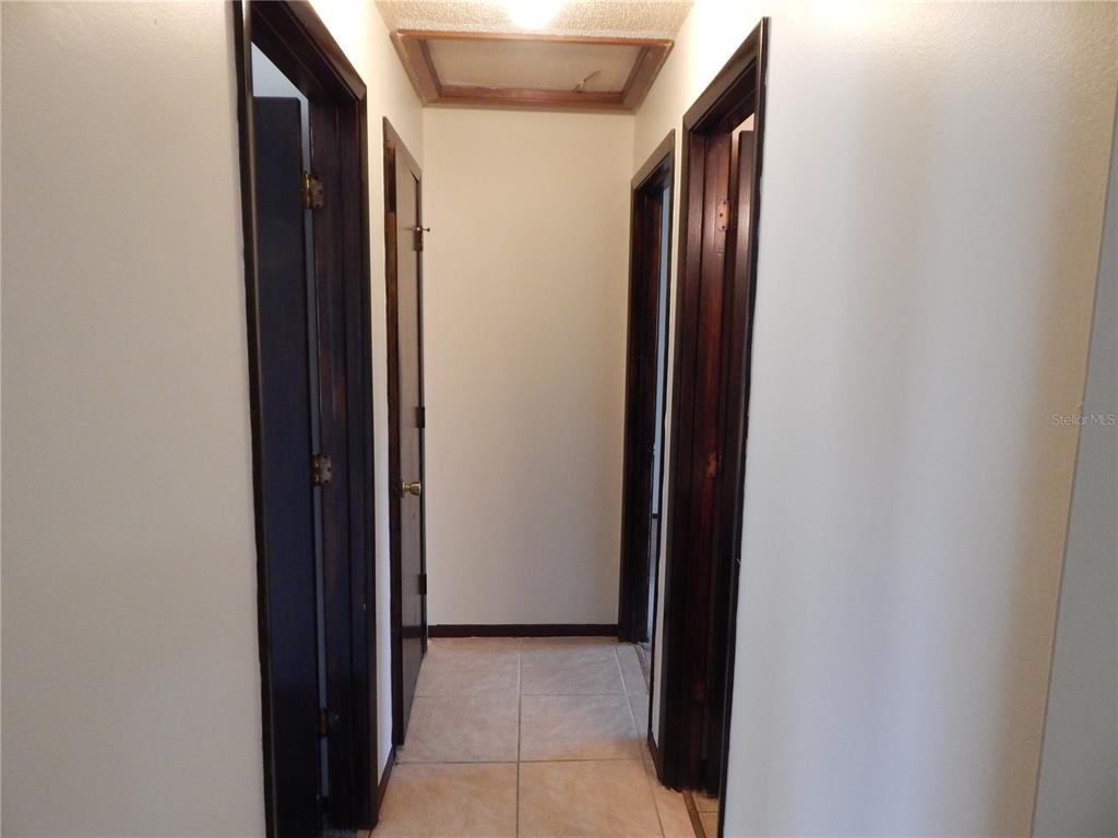 A narrow hallway features light tile flooring, white walls, and dark wood door frames — 2505 CORAL AVENUE, KISSIMMEE, FL