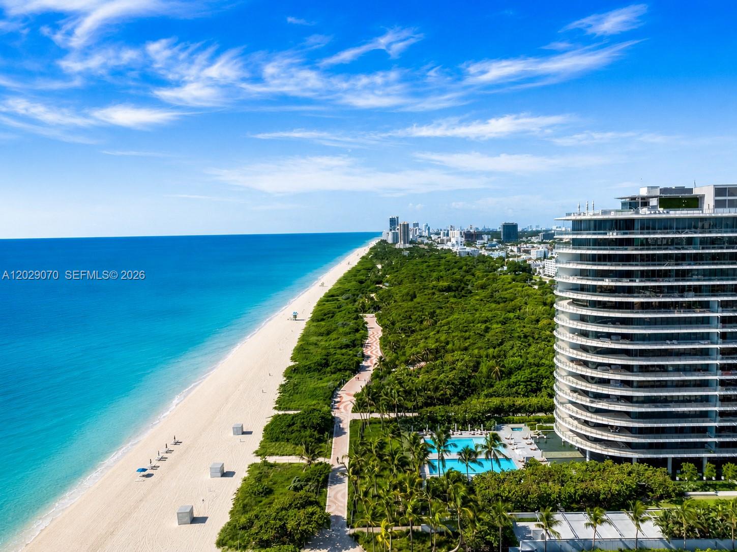 An aerial view shows a modern high-rise building next to a beach and forest — 8701 Collins Ave # 605, Miami Beach FL 33154, MIAMI BEACH, FL