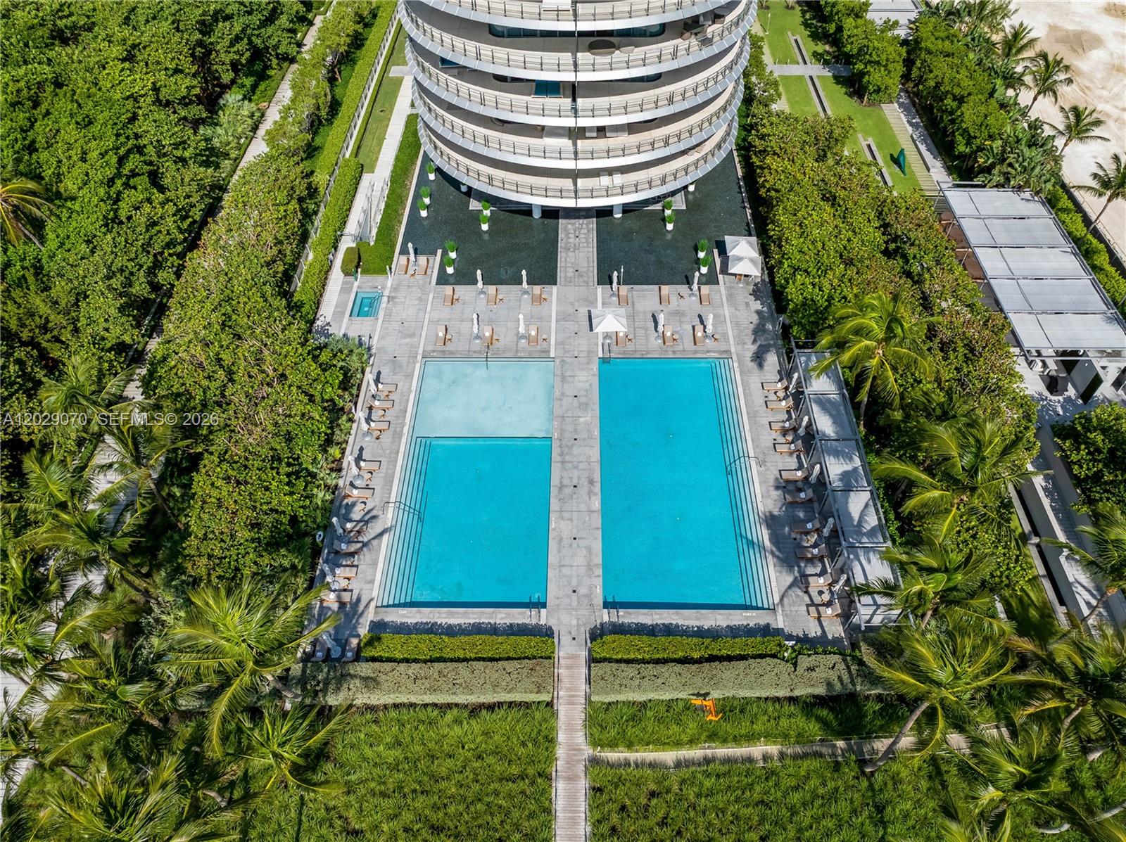 An aerial view shows a circular building with two rectangular swimming pools and lush landscaping — 8701 Collins Ave # 605, Miami Beach FL 33154, MIAMI BEACH, FL