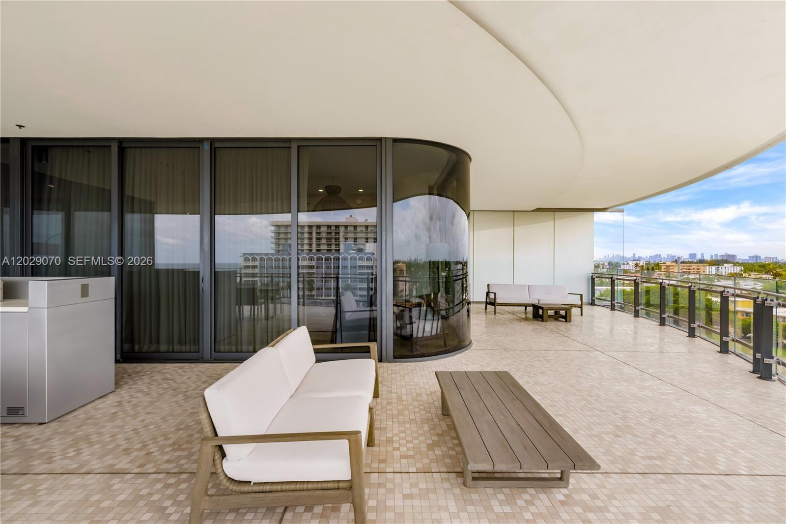 A spacious outdoor balcony features a curved glass wall, modern patio furniture, and city views — 8701 Collins Ave # 605, Miami Beach FL 33154, MIAMI BEACH, FL