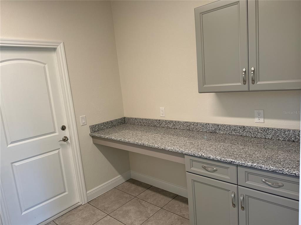 A laundry room features grey cabinets, a granite countertop, and a white door — 1449 MARJORIE LANE, NORTH PORT, FL