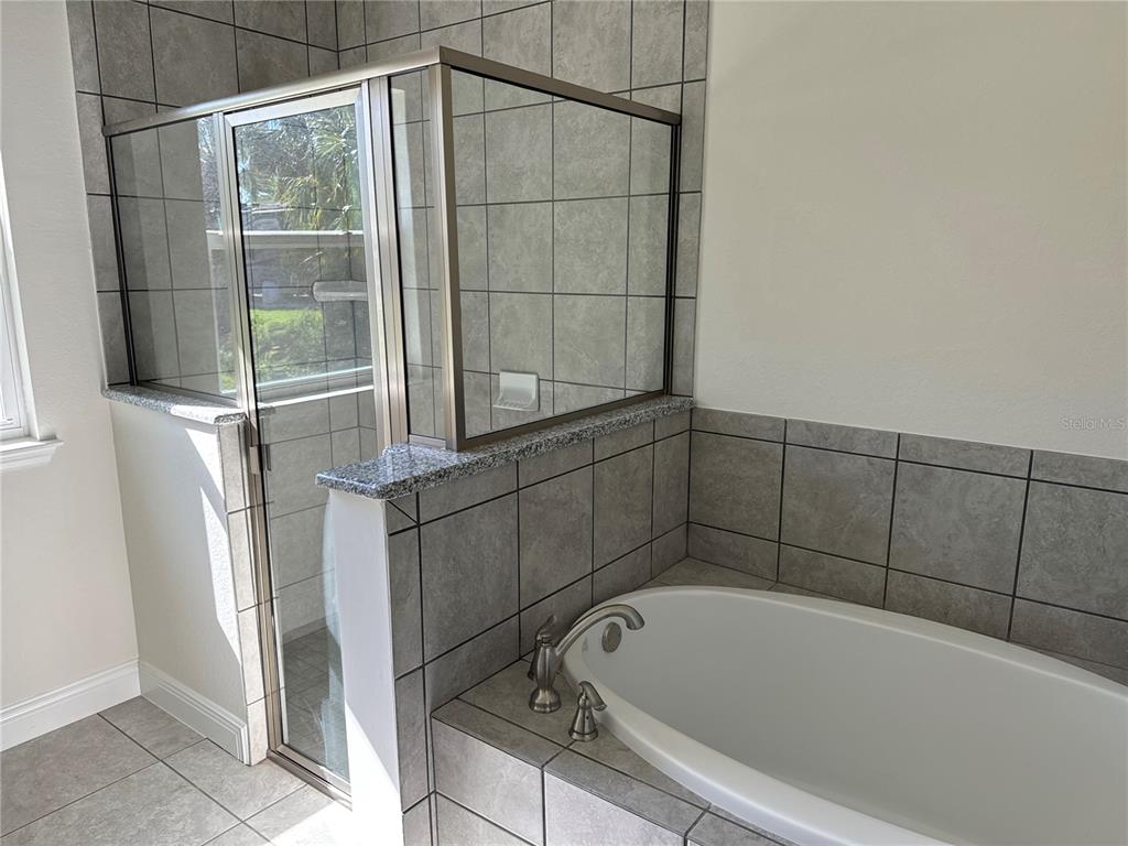 A bathroom features a tiled soaking tub and a separate glass-enclosed shower with gray tiles — 1449 MARJORIE LANE, NORTH PORT, FL