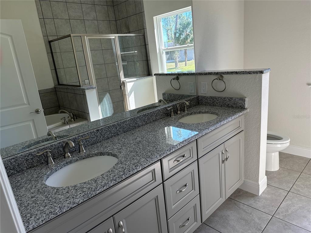 A bathroom features a double vanity with granite countertops, gray cabinets, and a tiled shower — 1449 MARJORIE LANE, NORTH PORT, FL