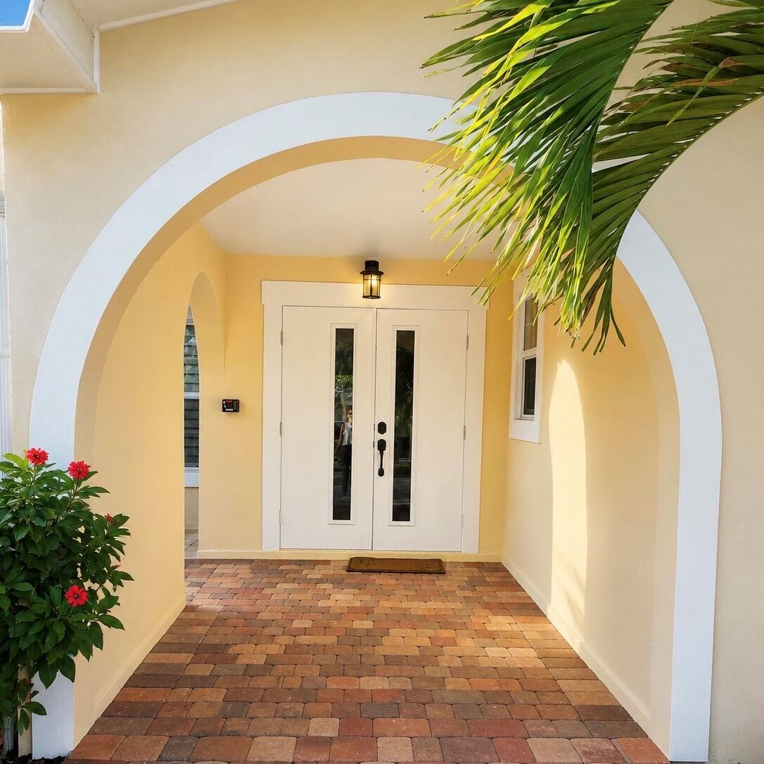A covered entryway with a brick paver floor, arched white trim, and double white doors — 1023 NW SPRUCE RIDGE Drive, Stuart FL 34994, STUART, FL