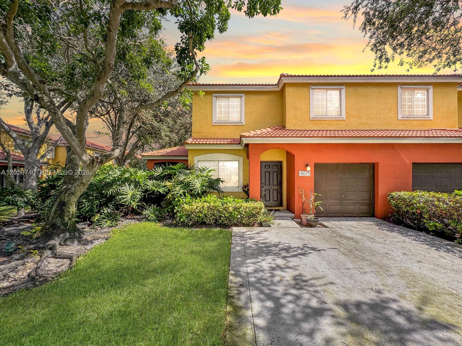 A two-story townhouse features yellow and orange stucco walls, a tile roof, and a driveway — 10341 SW 18th St, Miramar FL 33025, MIRAMAR, FL