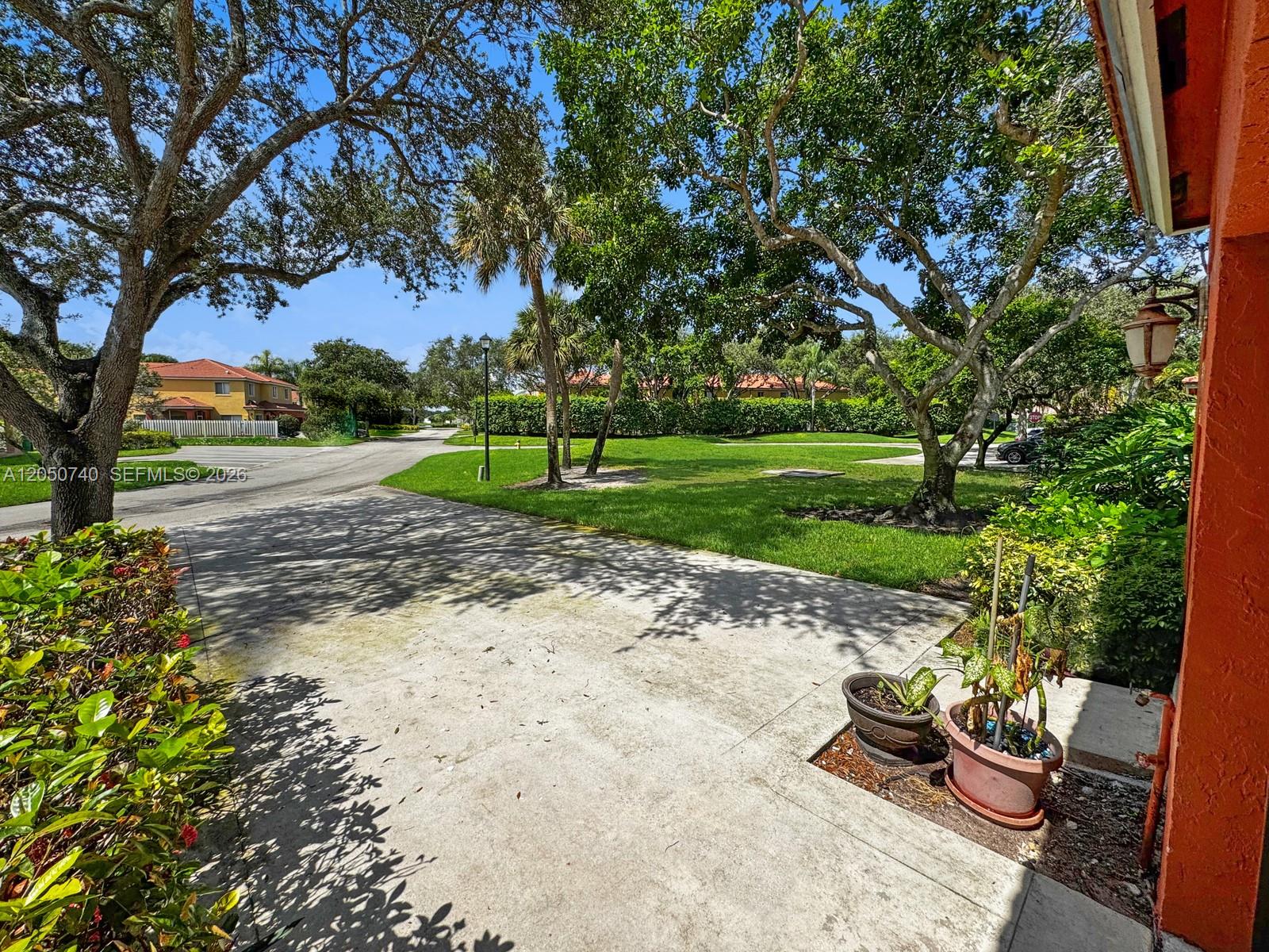 A concrete driveway leads to a grassy lawn surrounded by mature trees and residential buildings — 10341 SW 18th St, Miramar FL 33025, MIRAMAR, FL