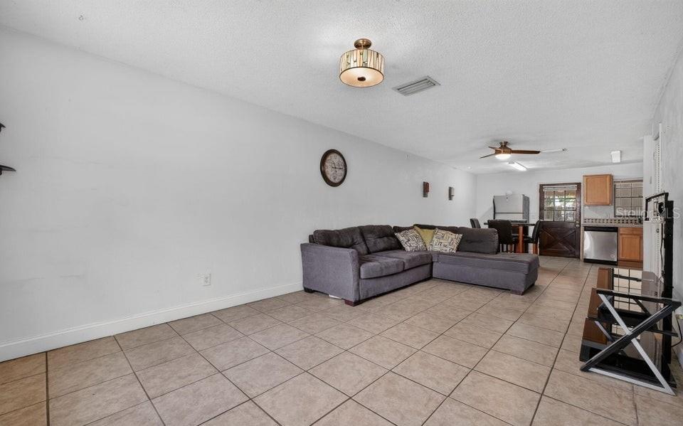 A living room with tile flooring, a gray sectional sofa, and an open kitchen area — 912 ROYAL OAK COURT, HOLLY HILL, FL