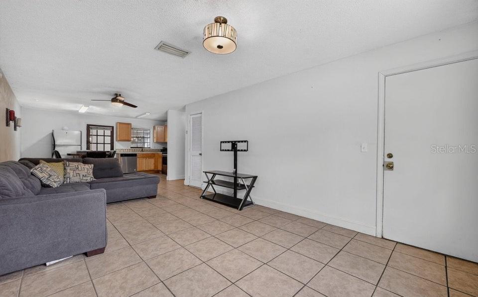 A living room with tile flooring, a gray sectional sofa, and an open kitchen area — 912 ROYAL OAK COURT, HOLLY HILL, FL