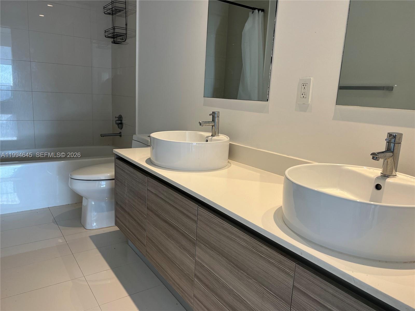 A modern bathroom features a double vanity with vessel sinks and a tiled bathtub area — 121 NE 34th St # 1207, Miami FL 33137, MIAMI, FL